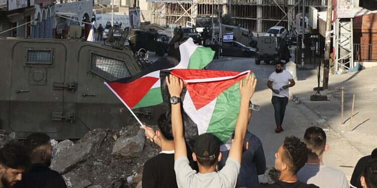 Israeli security forces stand blocking a road, separating between Jewish settlers entering the occupied-West Bank town of Huwara waving Israeli flags from their cars and Palestinians waving their national flag, on May 25, 2022. (Photo by JAAFAR ASHTIYEH / AFP)